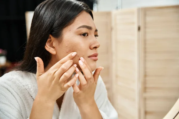Woman examining her skin and touching face with acne concerns before aesthetic treatment