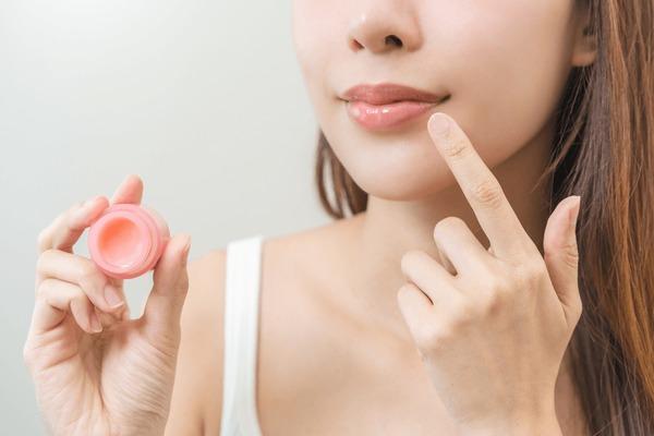 Woman applying lip balm from a small jar to moisturise her lips