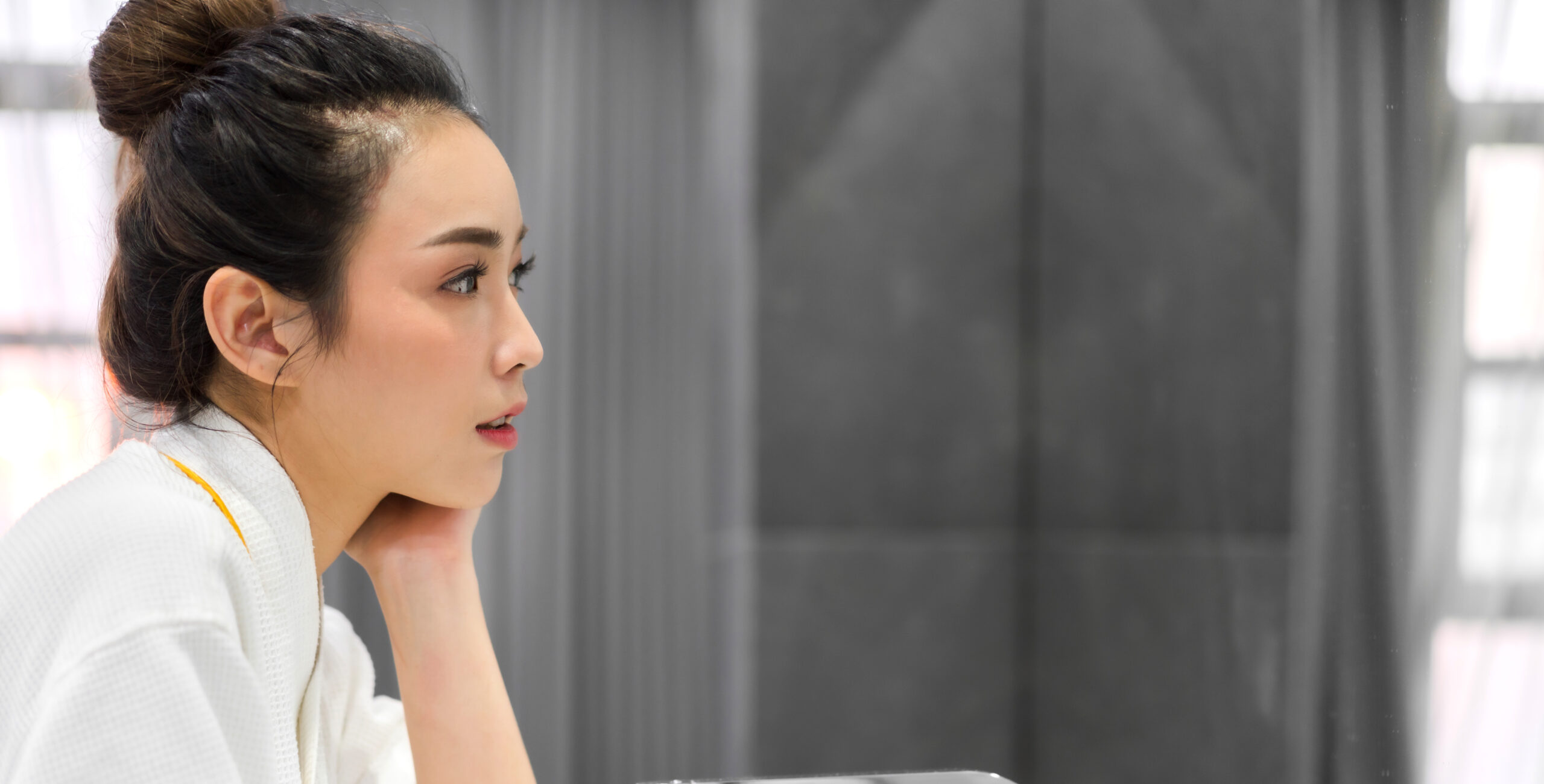 Asian woman examining her skin in the mirror, reflecting on facial care and skincare concerns