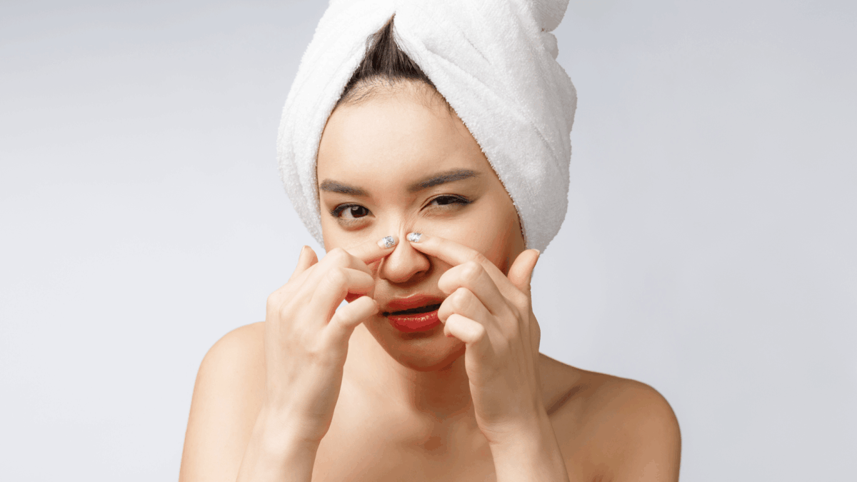 Asian woman looking at pimple on face and trying to remove it