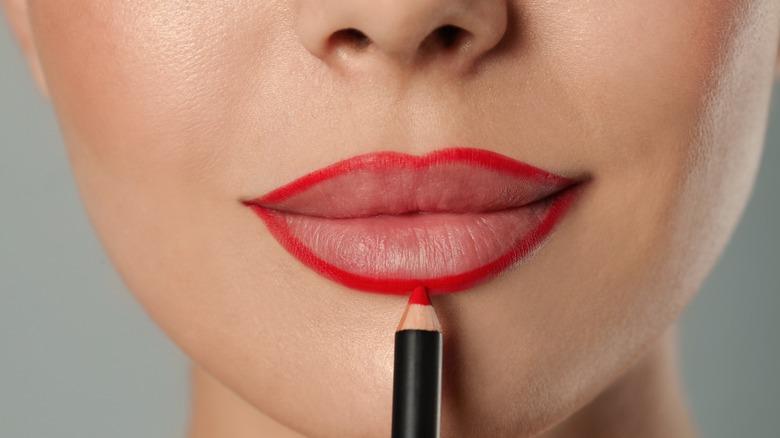 Close-up of woman outlining lips with red lip liner pencil