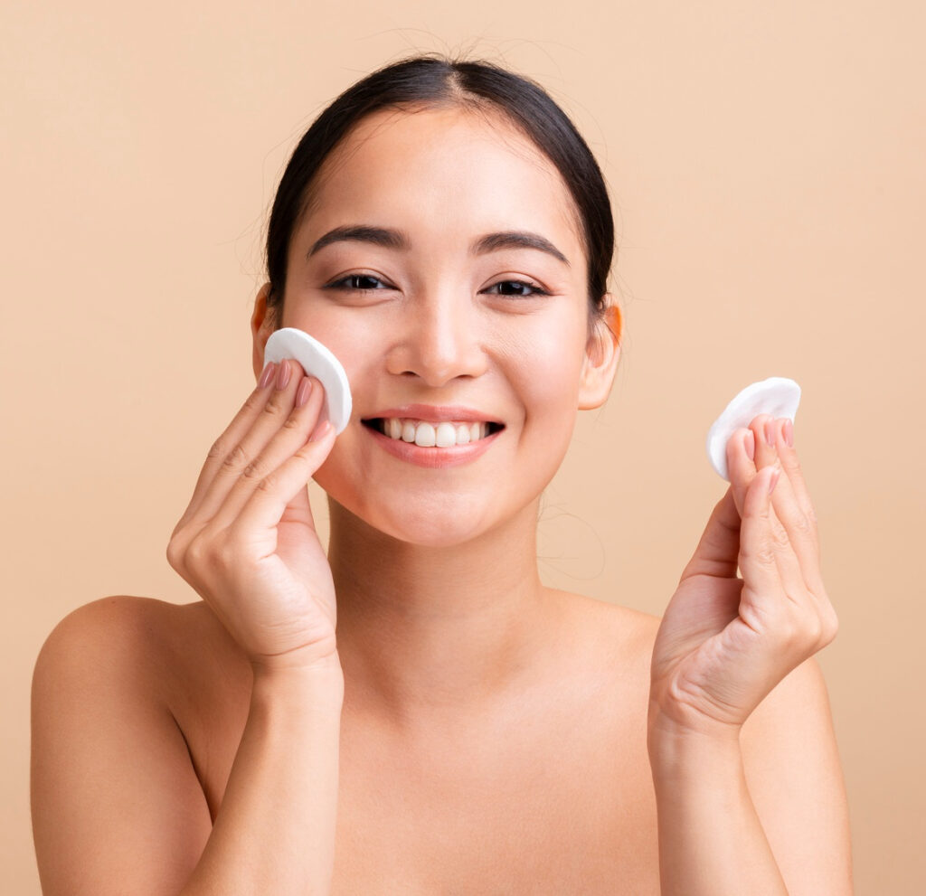 Smiling woman cleansing her face with cotton pads as part of her skincare routine